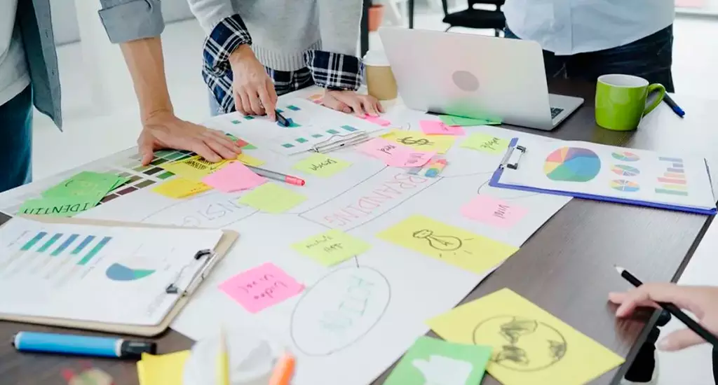Equipe de profissionais realizando uma sessão de planejamento estratégico com mapas, gráficos e post-its coloridos em uma reunião de trabalho.