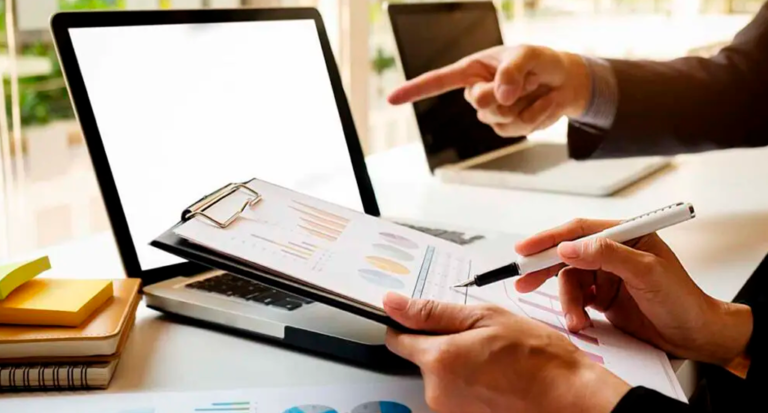 Pessoa apresentando análise financeira em uma reunião de negócios com gráficos e laptops na mesa.