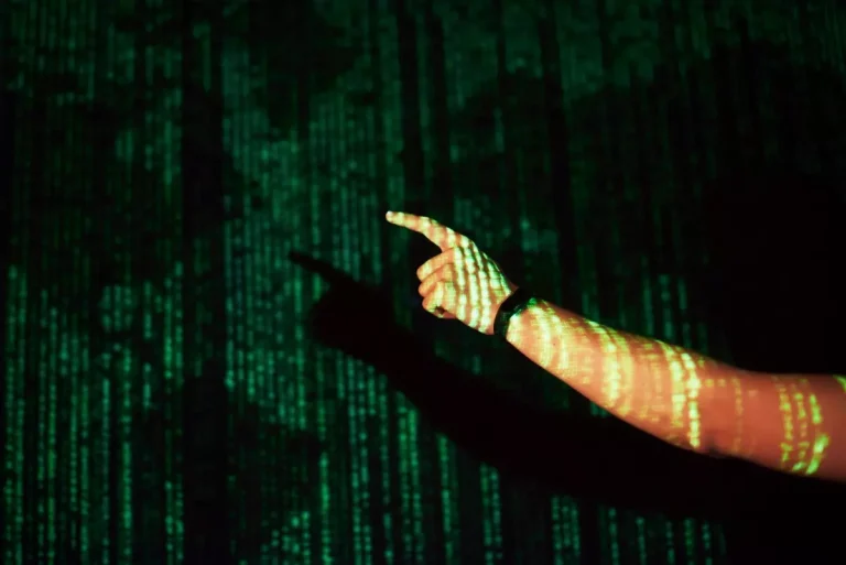 Mão com projeção de código digital, representando mudanças no algoritmo do Google, com efeitos de luz verde em fundo escuro.