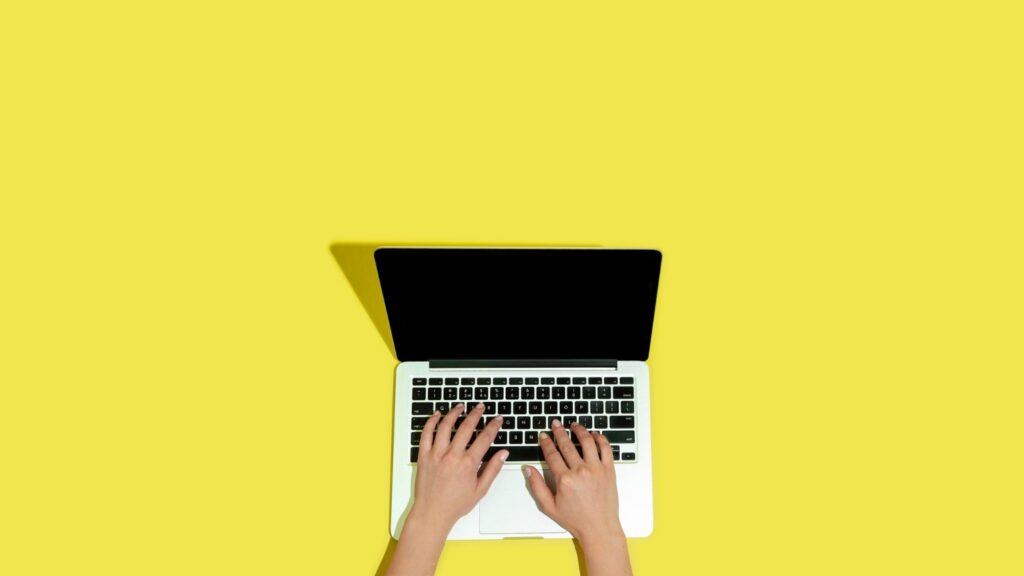 Imagem de uma pessoa usando um laptop, com fundo amarelo, destacando a importância da tecnologia, informática e trabalho remoto.