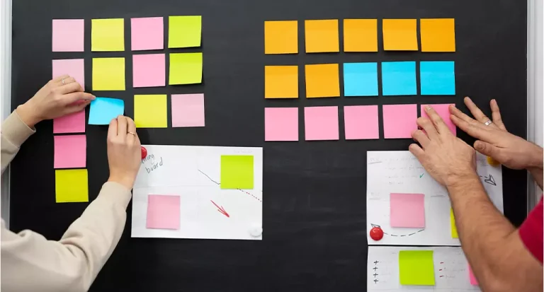 Pessoas organizando post-its coloridos em um quadro negro, ideal para sessões de brainstorming e planejamento de projetos.