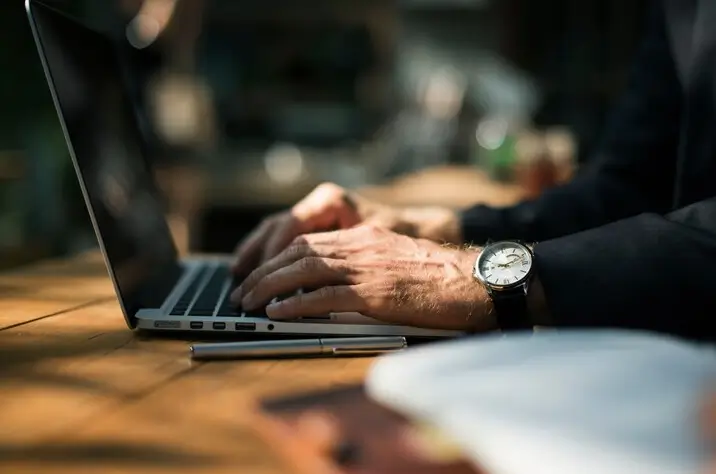 Pessoa digitando em um laptop, com foco na mão e no teclado, em um ambiente de trabalho, refletindo sobre o tamanho ideal de um post de blog.