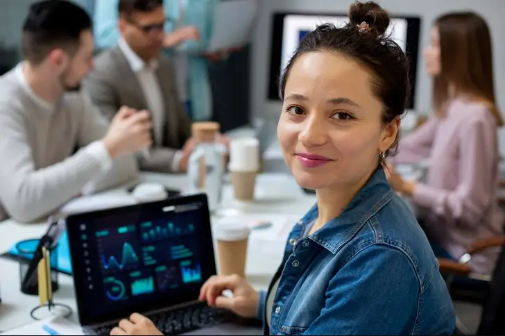 Profissional de marketing sorrindo em uma reunião de trabalho, com um laptop à sua frente exibindo gráficos e dados de SEO.