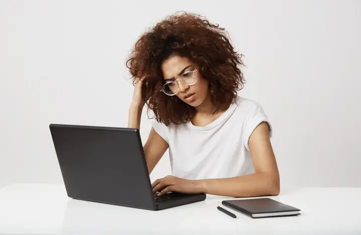 Mulher com cabelos cacheados e expressão de dúvida pensando sobre o que torna o SEO ruim, com laptop, caderno e caneta na mesa.