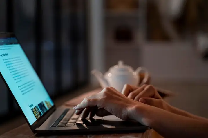 Mãos digitando em um laptop à noite, com foco na tela que exibe uma página web. A cena simboliza a pesquisa e otimização para descobrir Quais Plugins de SEO valem a pena para WordPress.
