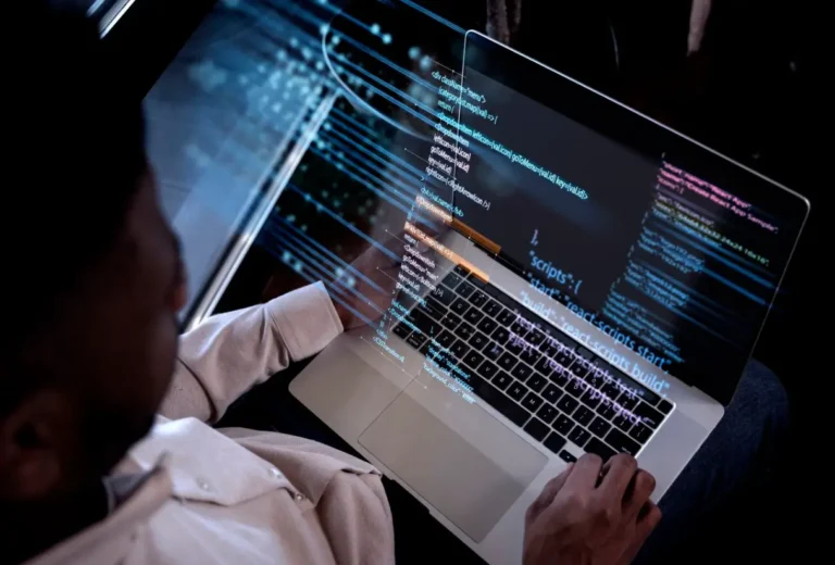 Um desenvolvedor, visto por cima do ombro, está trabalhando em um laptop. Códigos azuis e linhas de dados digitais brilham e flutuam acima da tela, simbolizando tecnologia avançada ou realidade aumentada.