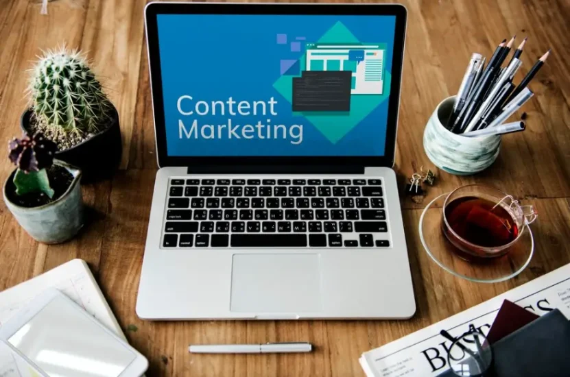 Imagem de um laptop exibindo conteúdo de marketing de conteúdo, ao lado de canetas, cacto, chá e documentos, ideal para estratégias de Content Marketing.