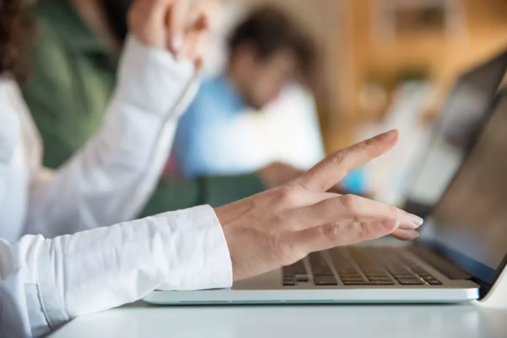 Uma foto em close das mãos de uma pessoa digitando em um teclado de laptop, sugerindo trabalho ou estudo.