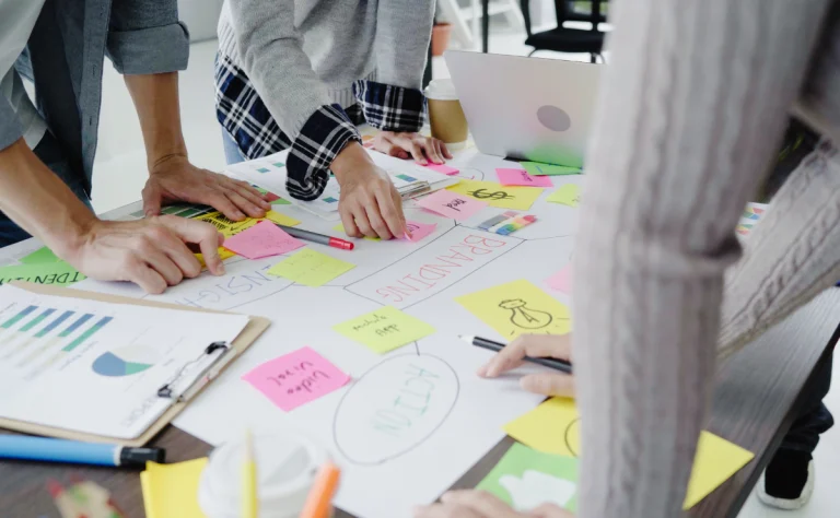 Equipe de profissionais analisando estratégias de conteúdo em uma reunião, com várias notas adesivas, gráficos e um laptop sobre a mesa, para saber se a estratégia de conteúdo está funcionando