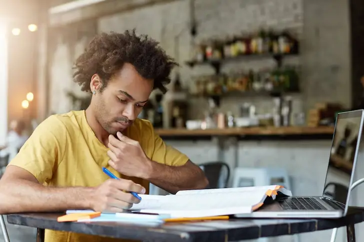 Homem pensativo estudando como se manter atualizado em SEO em 2025 com computador portátil e livros em ambiente de café ou escritorio, demonstrando foco e concentracao