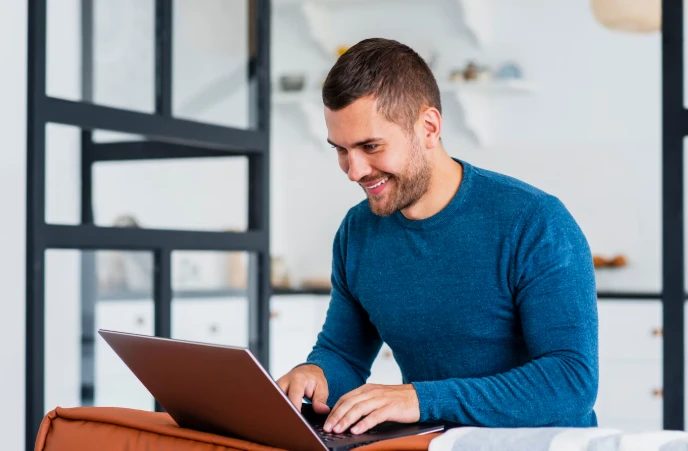 Homem sorridente usando um laptop em um ambiente moderno, ideal para trabalhos remotos ou estudo em home office, com foco em tecnologia e produtividade.
