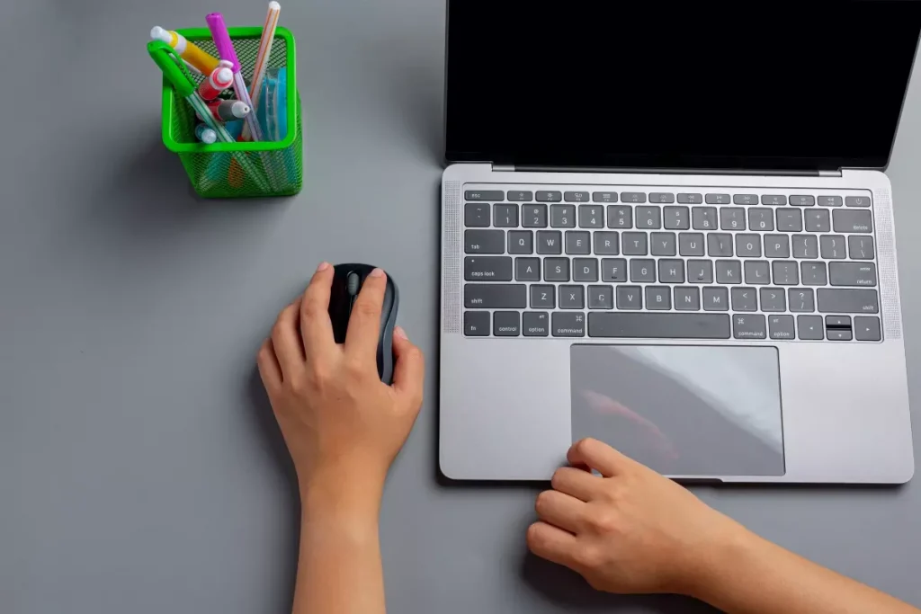 Imagem de um laptop, uma mão usando mouse, e uma caneca com itens de escritório em uma mesa cinza, apresentando o tema de SEO on page e off page.