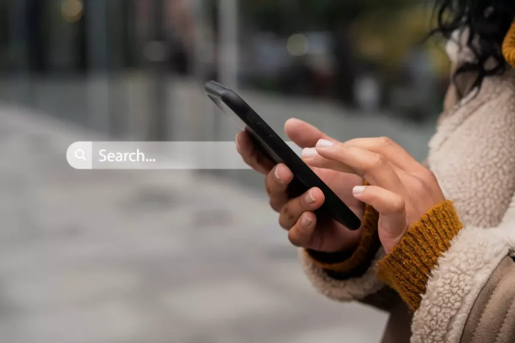 Pessoa usando smartphone ao ar livre buscando informações sobre seo para dispositivos móveis.