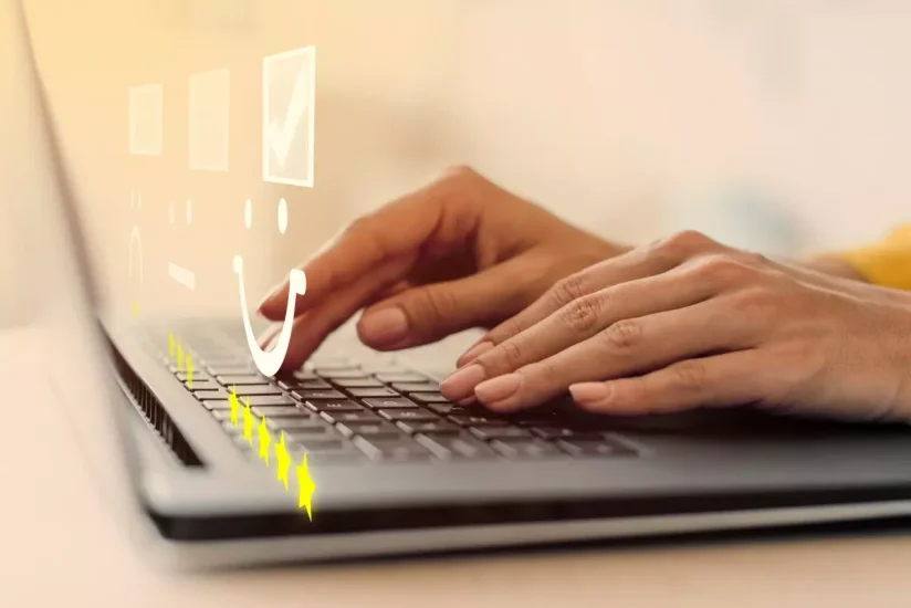 Mãos digitando em um notebook com ícones digitais de avaliação por estrelas e um rosto sorridente projetados acima do teclado, representando satisfação do usuário ou feedback positivo.