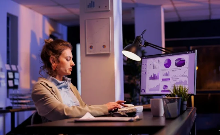 Uma mulher jovem, de perfil, trabalha concentrada em um escritório moderno durante a noite.